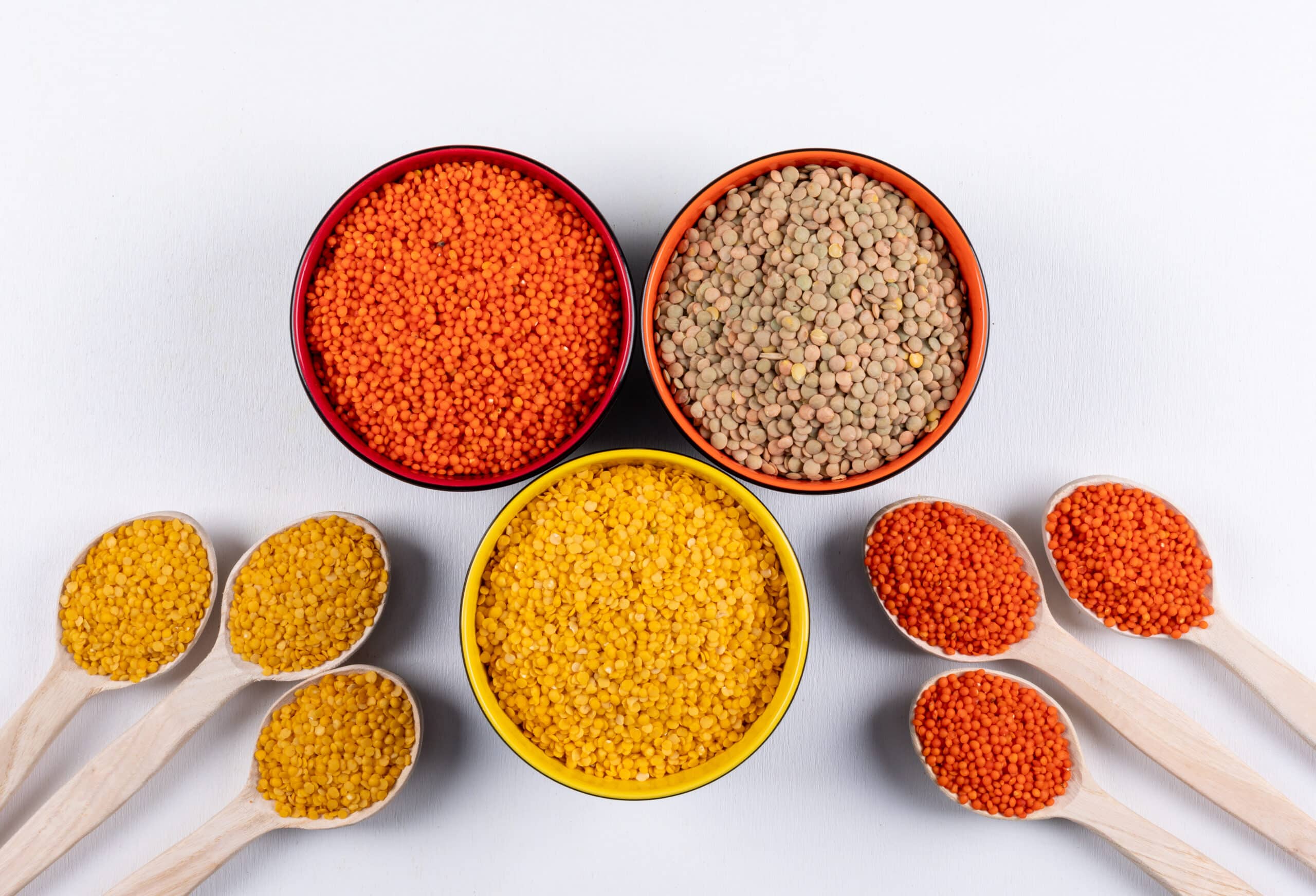 Yellow and red lentils in a wooden spoons and different colored bowls on a white background. top view.